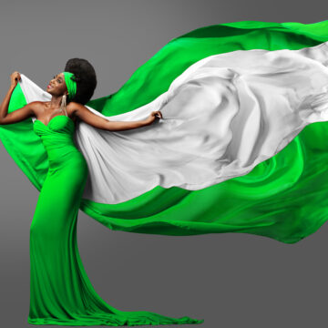 Woman dancing with Nigerian Flag in Green White Dress. Fashion Model with Afro Hair in Long Gown with flying Silk Scarf. Waving Chiffon Fabric over Gray. Nigeria Independence Day FG Declares Thursday 1st October, Public Holiday